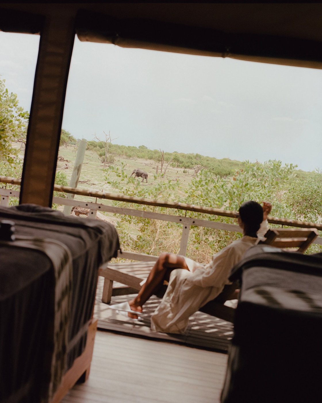 Guest reclining on a daybed in open-air room overlooking the plains at Belmond Savute Elephant Lodge