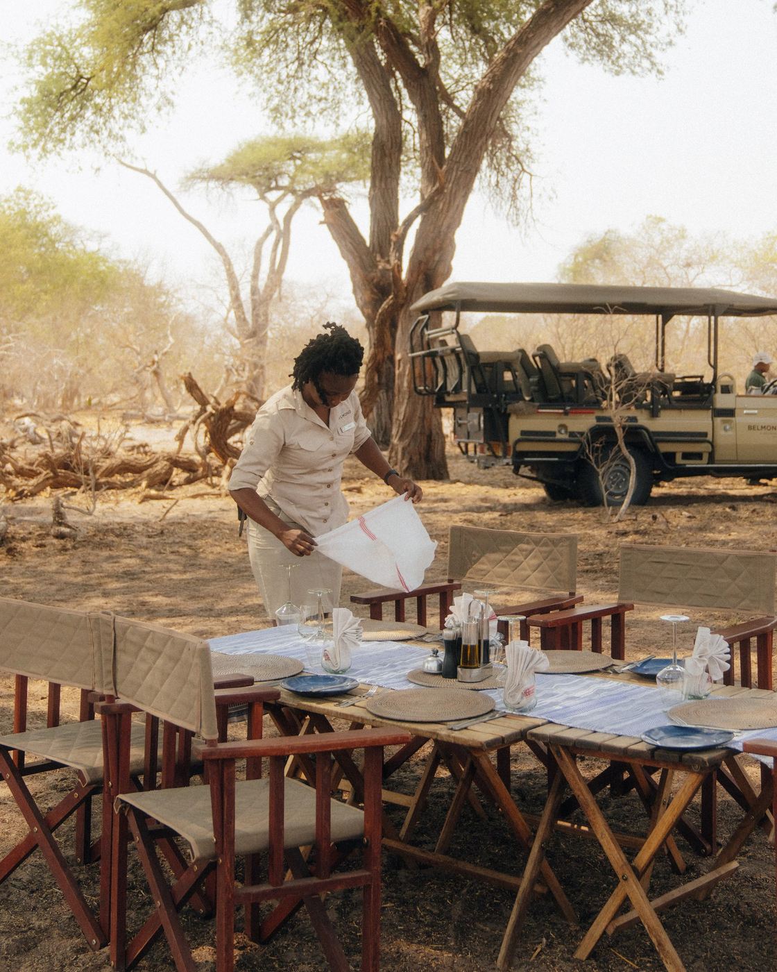 Staff setting an outdoor dining table in the bush at Belmond Savute Elephant Lodge