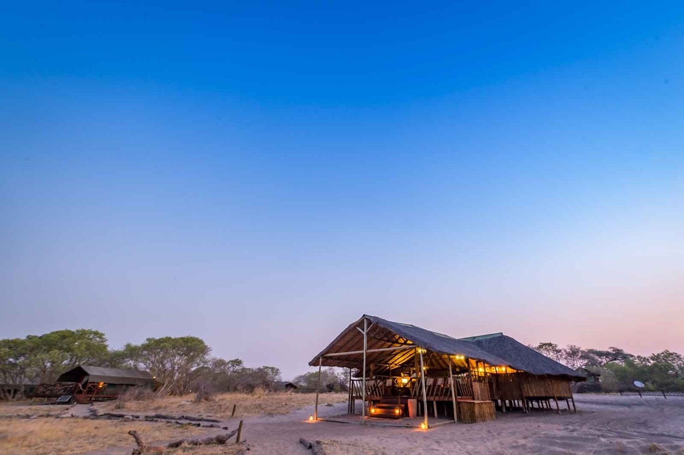 Thatched camp deck glowing at dusk among trees at Camp Savuti, Chobe