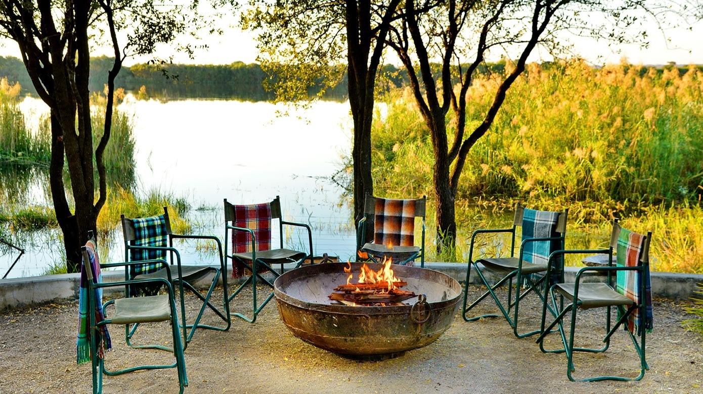 Fire pit and lounge chairs on a deck overlooking the water at Chobe Bakwena Lodge