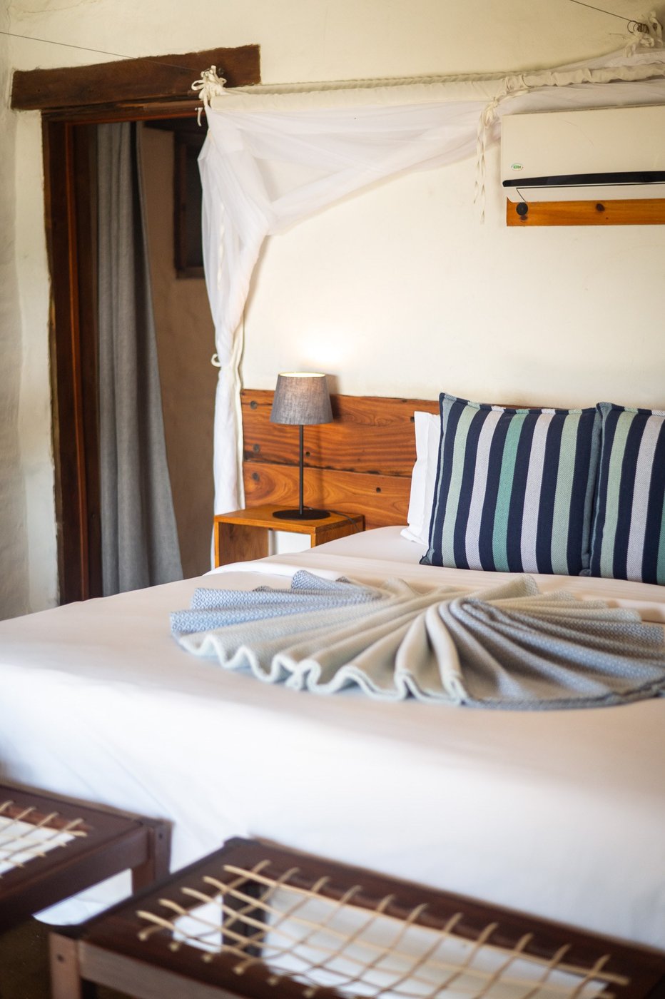 Canopy bed with striped cushions in a thatched room at Chobe Elephant Camp