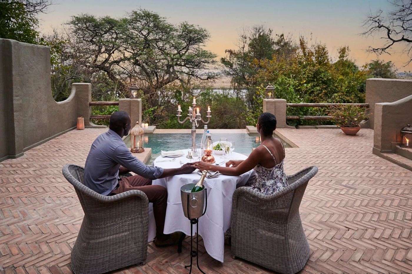 Couple holding hands at a candlelit poolside dinner at Chobe Game Lodge