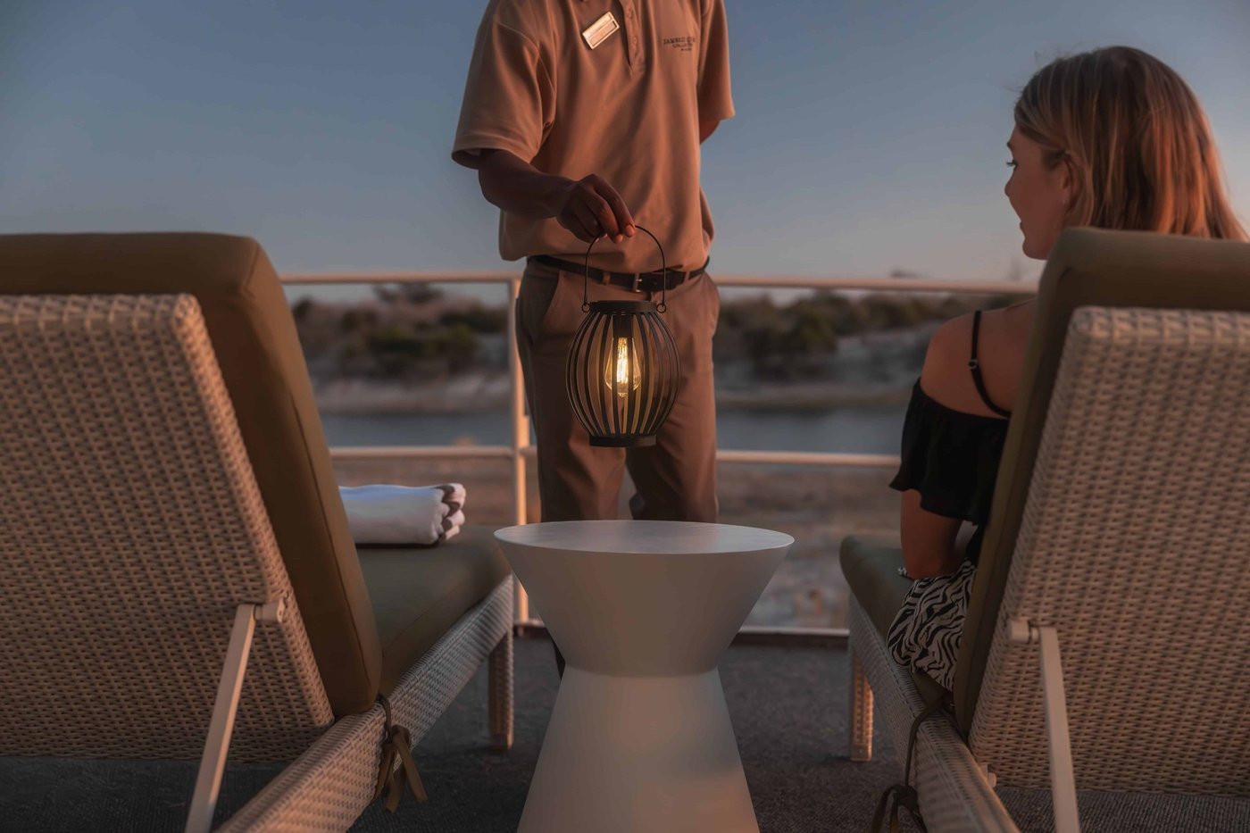 Staff lighting a lantern for guests at sunset at Chobe Princess