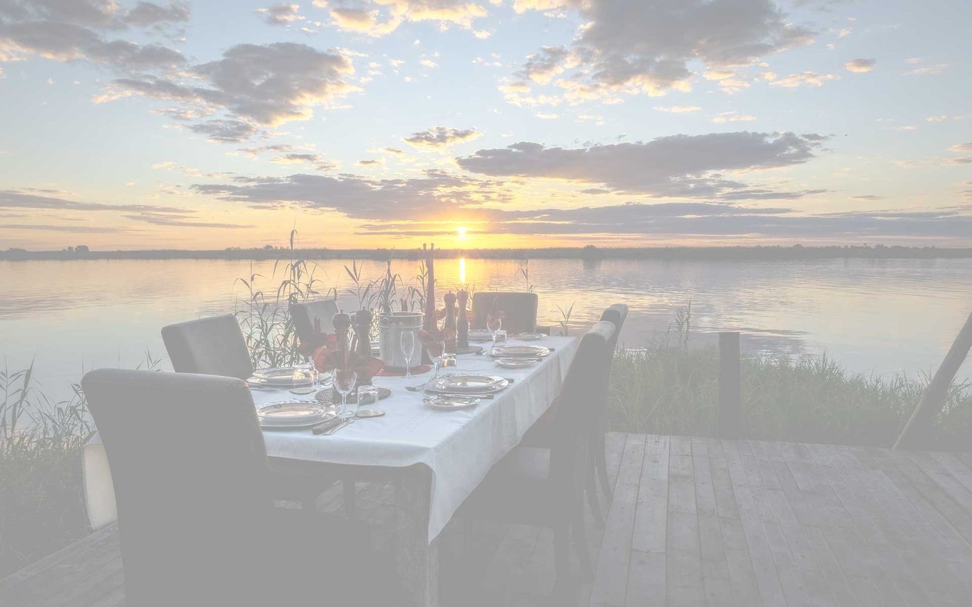 Dining table set on the deck at sunset over the water at Chobe River Lodge, Chobe