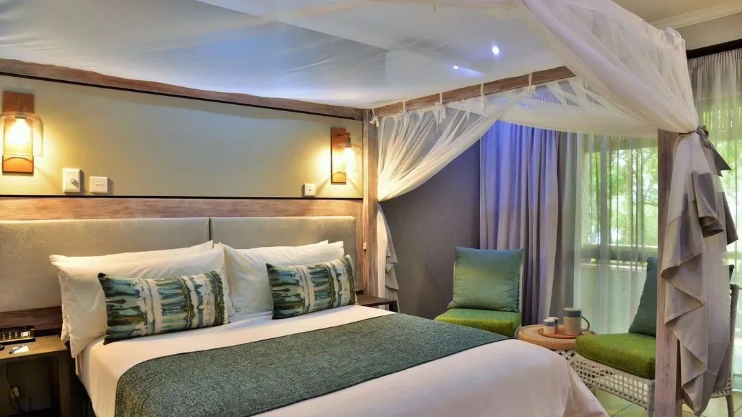 Canopy bed with teal accents in a guest room at Cresta Mowana Safari Resort & Spa