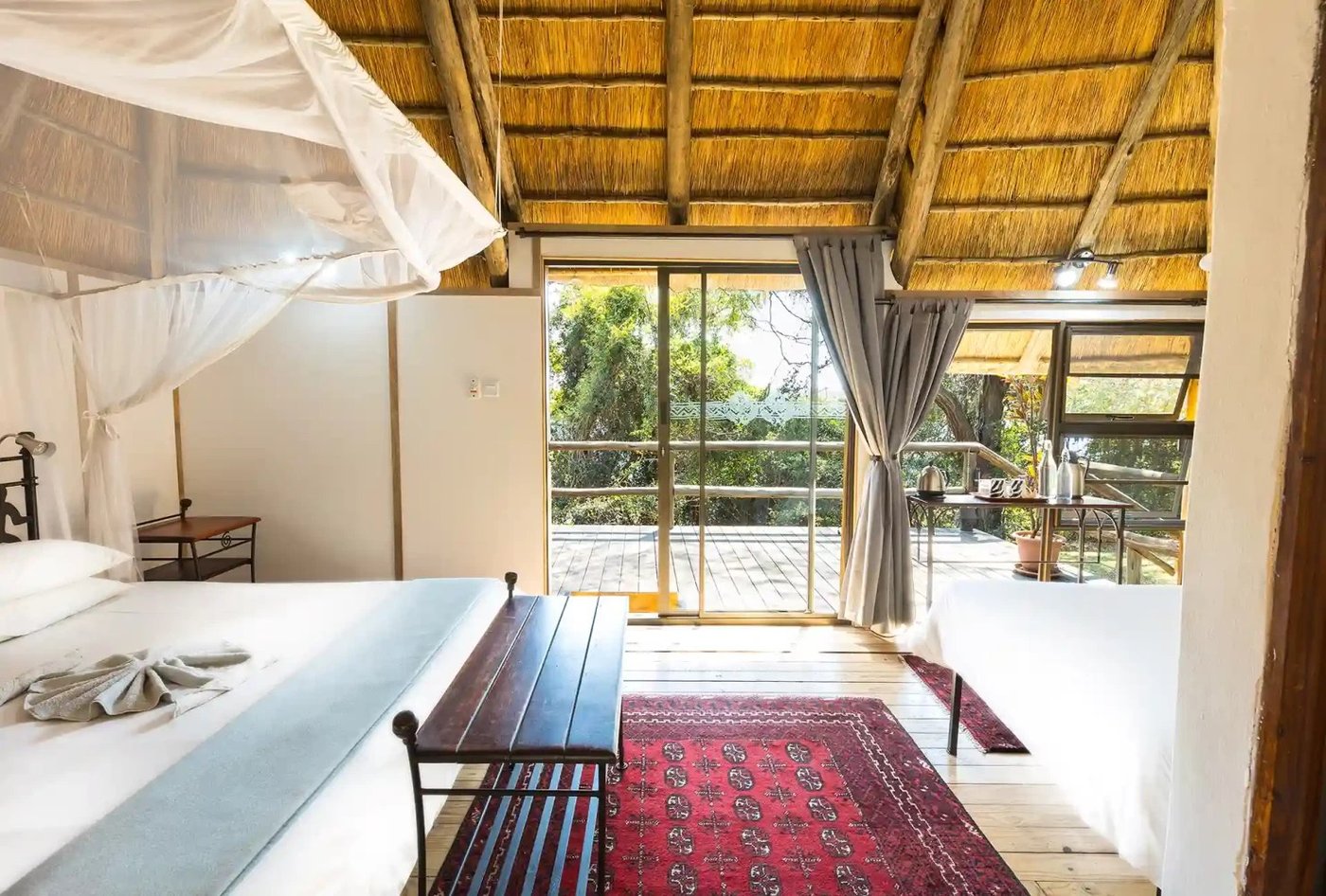 Bedroom opening onto a private patio under a thatched roof at Kubu Lodge