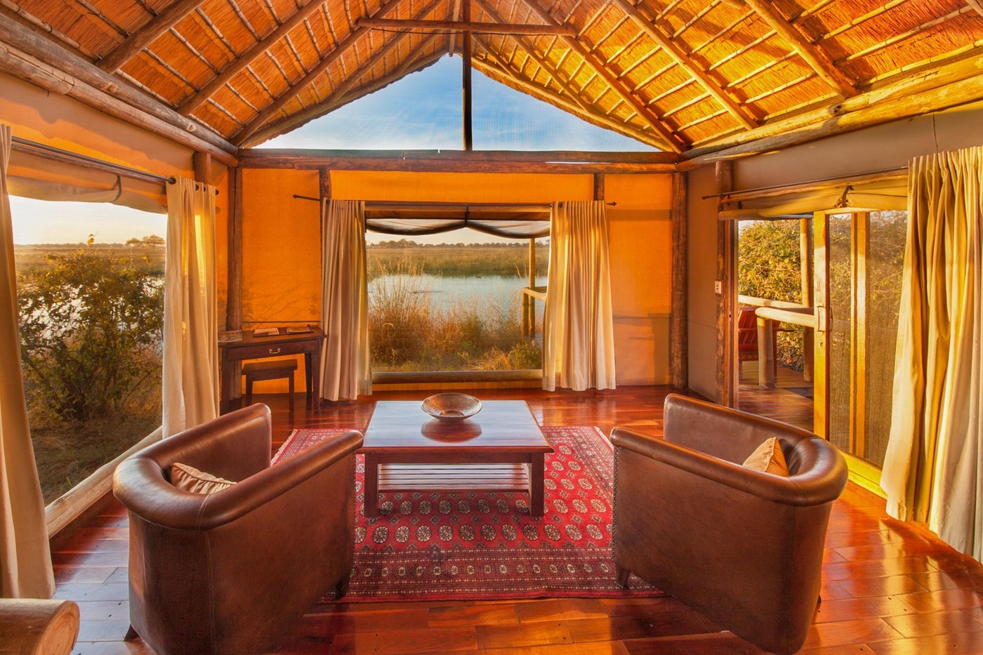 Lounge with leather chairs overlooking the river through large windows at Lagoon Camp