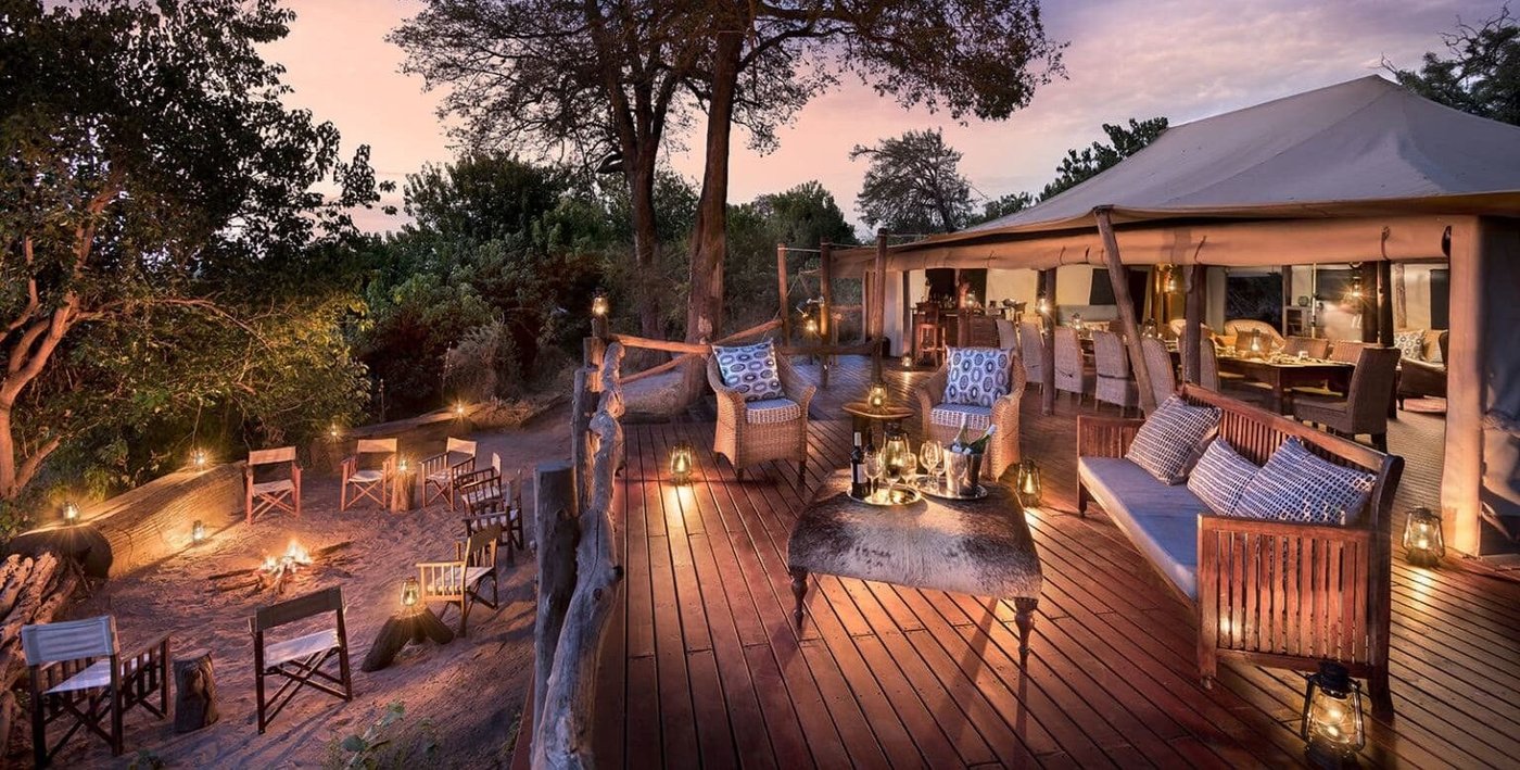 Deck with lounge chairs lit by lanterns at dusk at Linyanti Bush Camp, Chobe