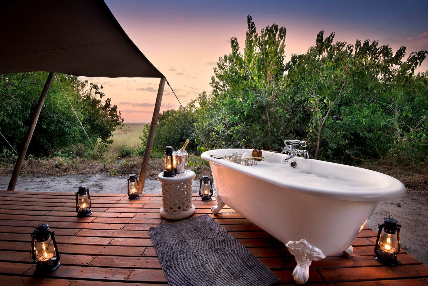Outdoor bathtub on the deck lit by lanterns at dusk at Linyanti Bush Camp