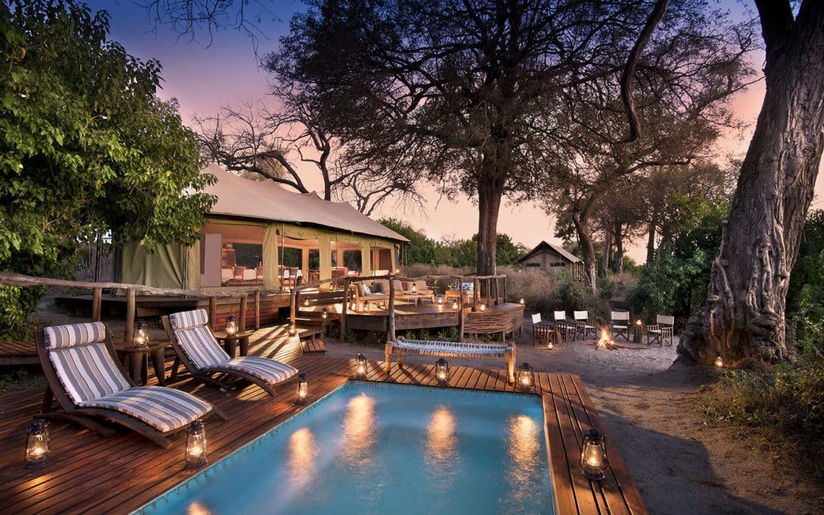 Pool deck lit by lanterns at dusk among the trees at Linyanti Ebony, Chobe