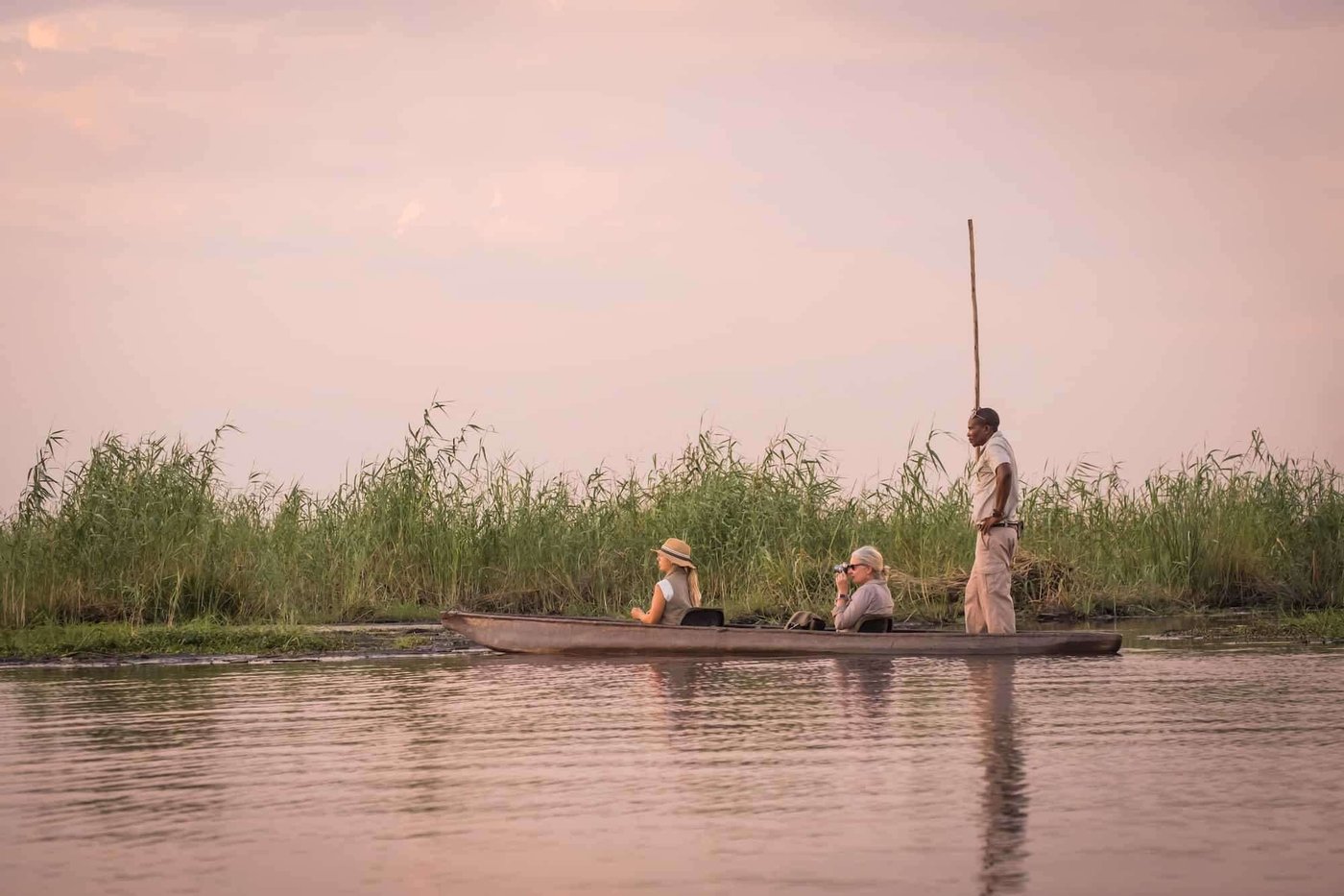 Guide poling a mokoro canoe with guests at dusk near Linyanti Ebony