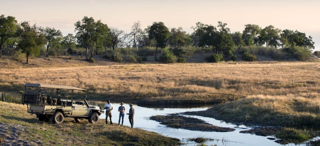 Safari vehicle with guests beside a water channel at Linyanti Expeditions
