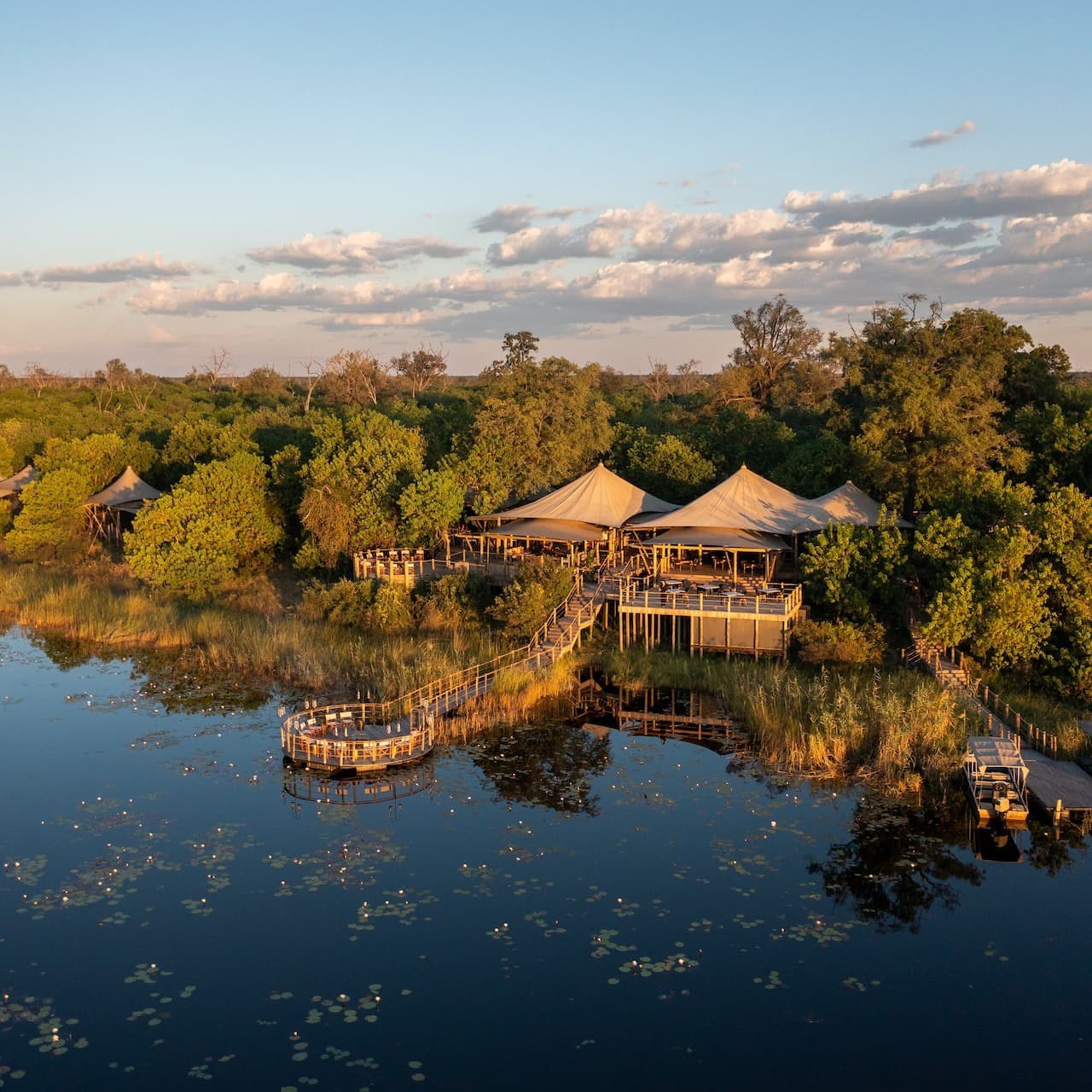 Aerial view of the tented camp reflected in the floodplain at dusk at Little DumaTau, Chobe