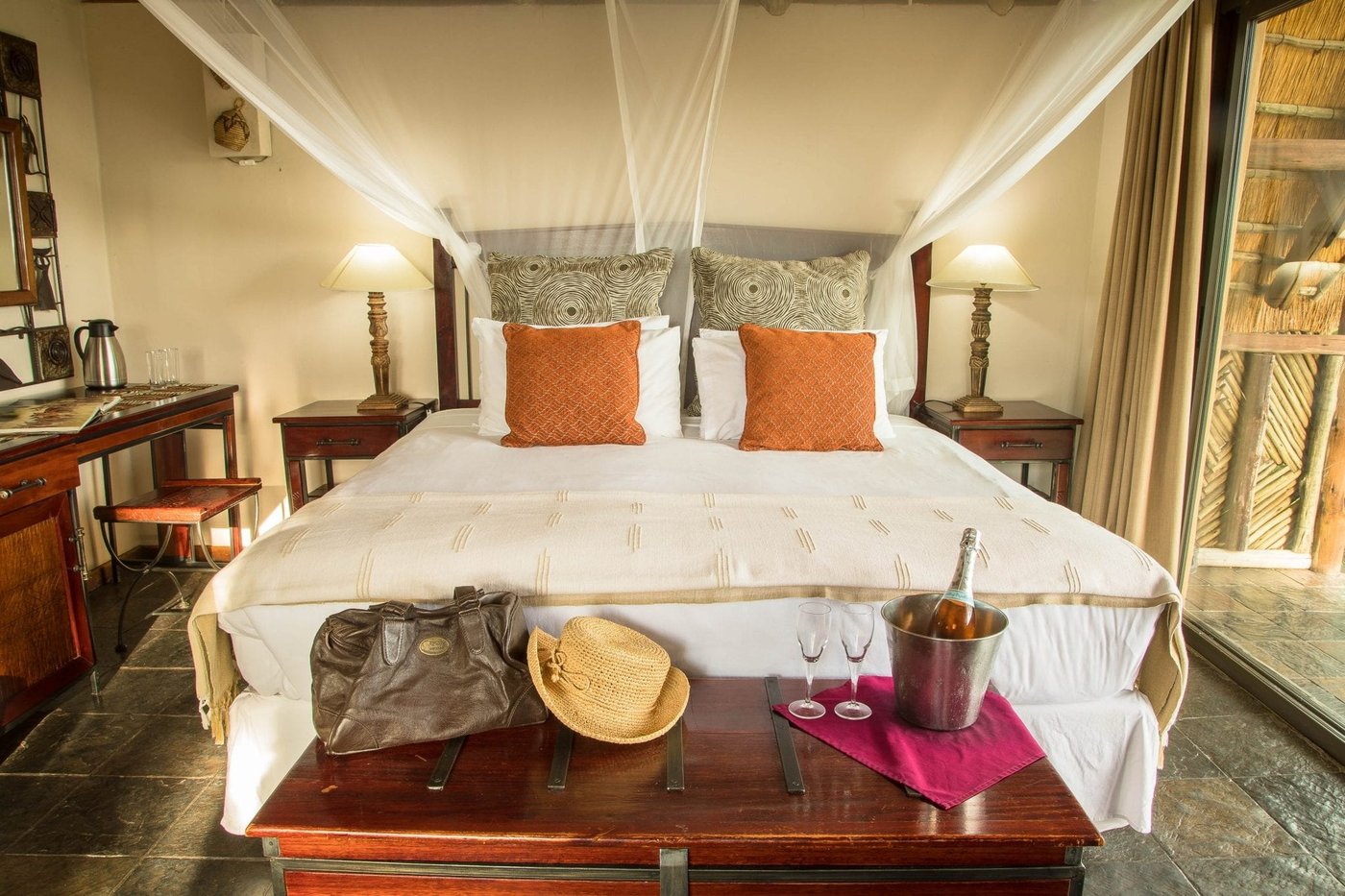 Bedroom with orange cushions and a chilled wine bucket at Muchenje Safari Lodge