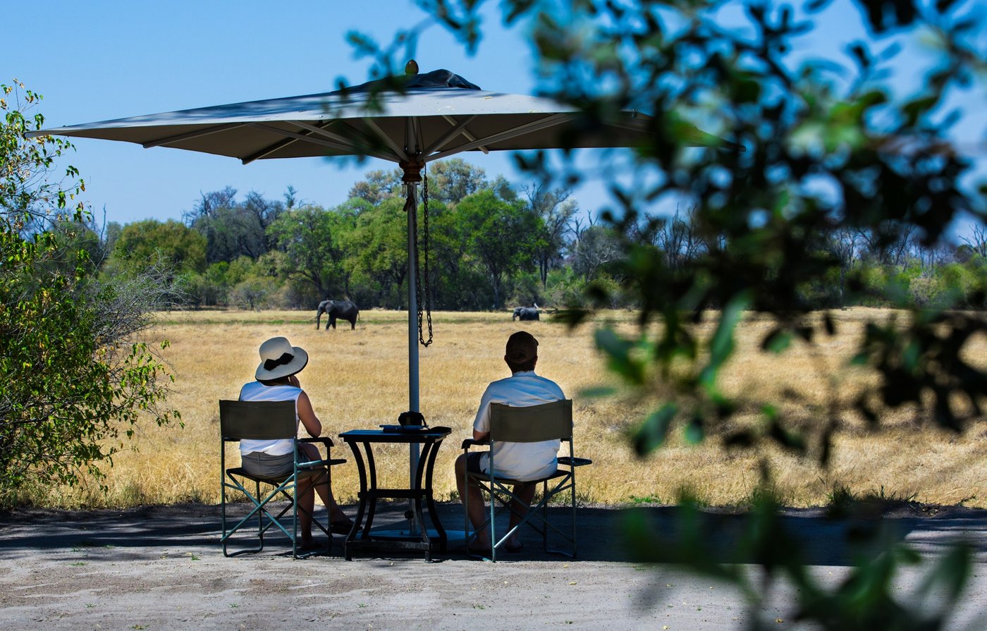 Guests relaxing under an umbrella watching elephants near Ngoma Safari Lodge, Chobe