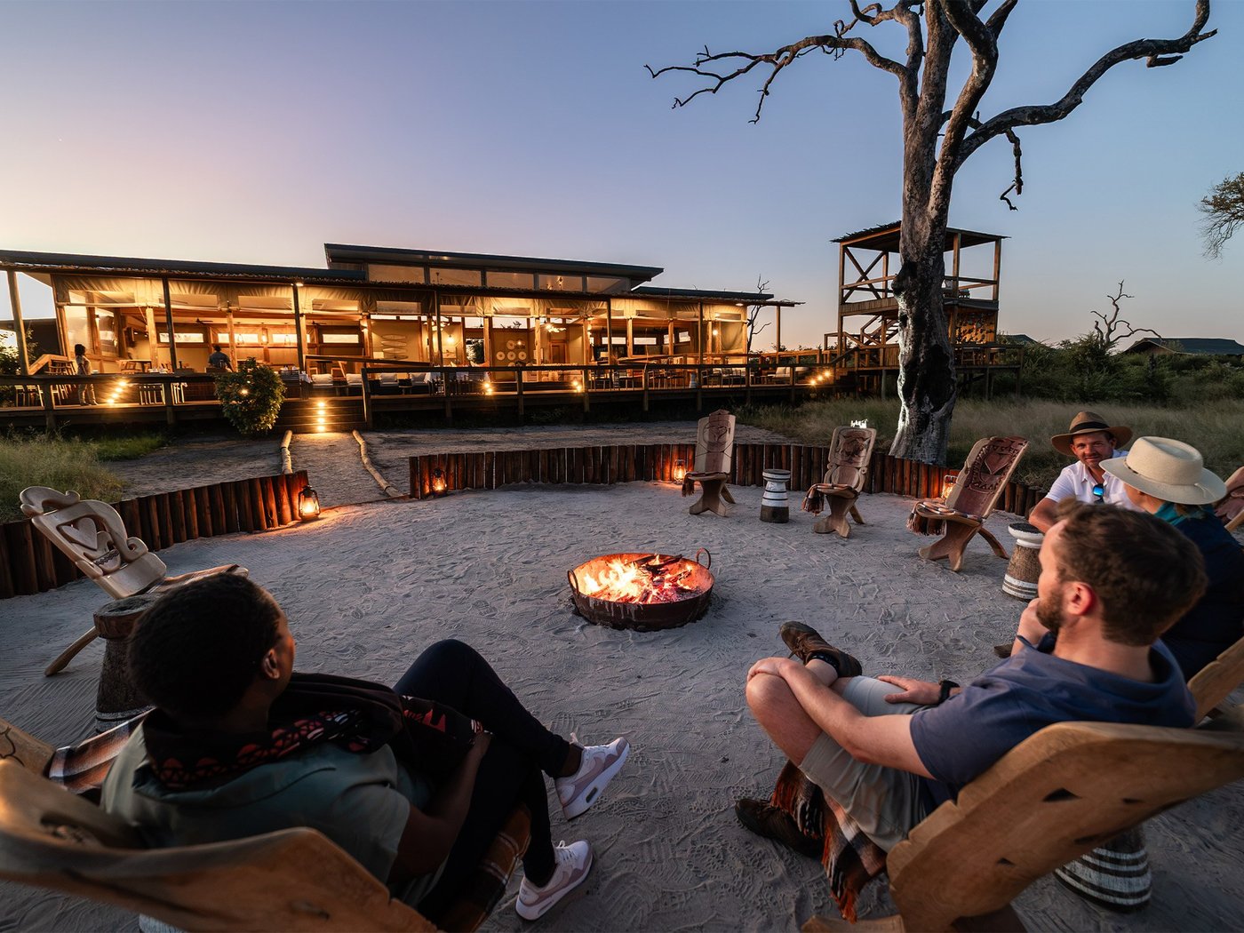 Campers gathered around a fire pit at dusk near Nogatsaa Campsite, Chobe