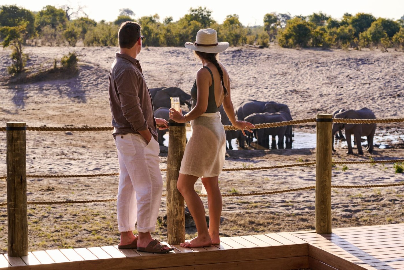 Couple watching elephants at the waterhole from the deck at dusk at Savute Safari Lodge