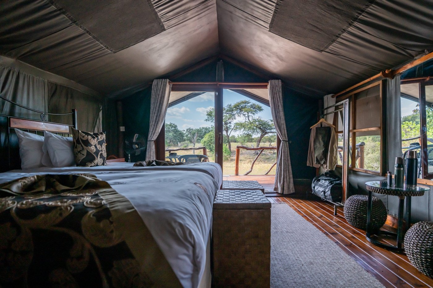 Tent interior with a bed and a large window view at Savuti Campsite