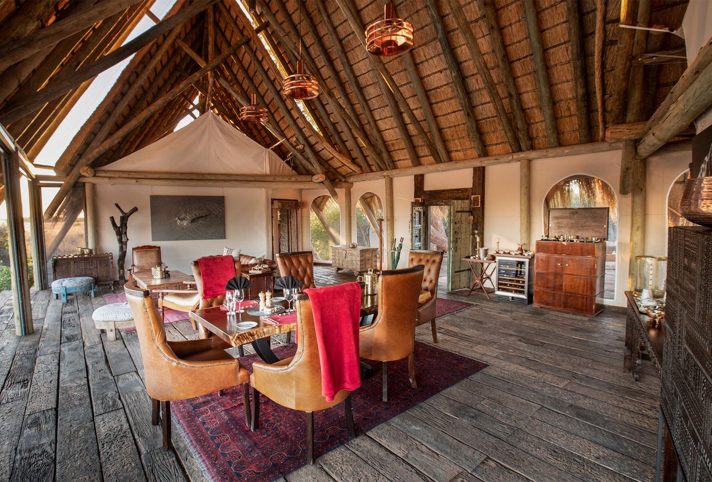 Dining area with red-draped chairs under a thatched roof at Selinda Camp