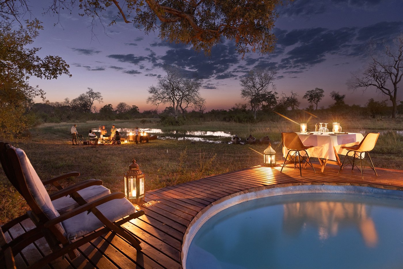 Dining table set beside the pool at dusk at Selinda Explorers Camp