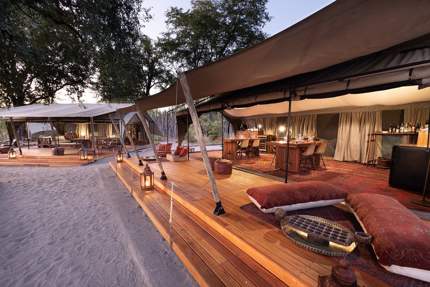 Canvas-roofed lounge deck with leather poufs on the sand at Selinda Explorers Camp