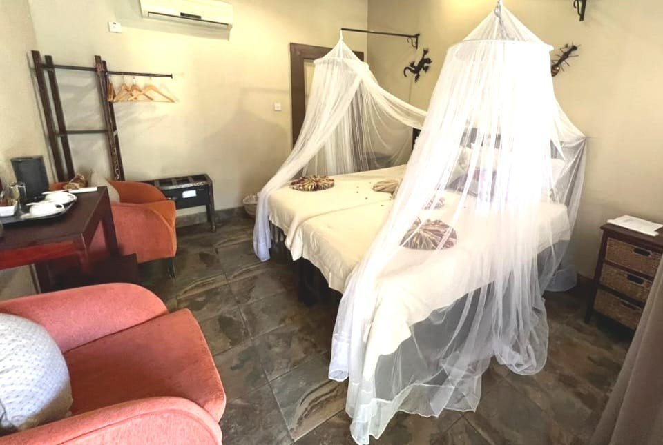 Renovated bedroom with red armchairs and a canopy bed at Thebe River Safaris