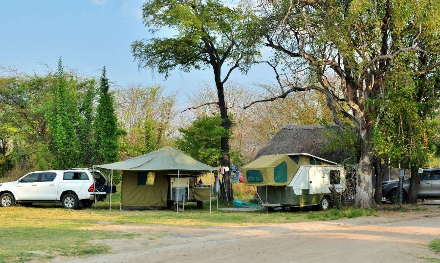 Campsite with a tent, trailer and vehicle among trees at Thebe River Safaris