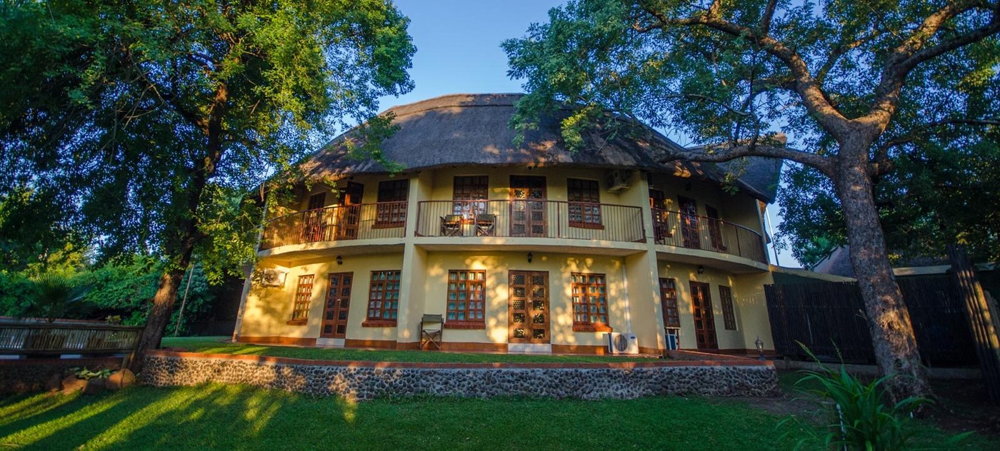 Lodge building lit at dusk among trees at Water Lily Lodge, Chobe